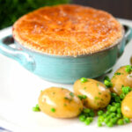 Pork and apple pie with a puff pastry lid served with buttered new potatoes and peas.