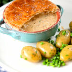 Pork belly and apple pie with a puff pastry lid (partially removed) with potatoes and peas.