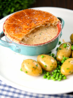 Pork belly and apple pie with a puff pastry lid (partially removed) with potatoes and peas.