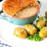 Pork belly and apple pie with a puff pastry lid (partially removed) with potatoes and peas.