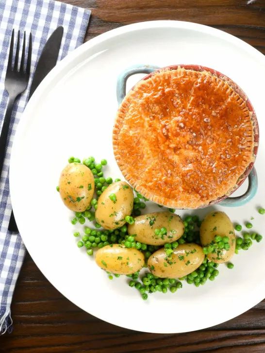 Overhead pork and apple pie with a puff pastry lid served with buttered new potatoes and peas.