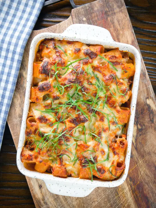 Overhead cheesy baked pasta al forno with a beef, pork and tomato sauce garnished with fresh basil.