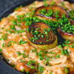 Close-up creamy balsamic leek and mushroom risotto topped with seared leek rings.