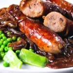 Close up bangers and mash with onion with cut uopen sausages showing cooked texture.