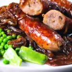 Close up bangers and mash with onion with cut open sausages showing cooked texture.