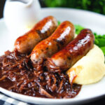 Bangers (sausages) and mash with onion gravy, peas and runner beans.