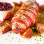 Close-up cranberry and brie stuffed chicken wrapped in bacon with braised chicory and fried potatoes