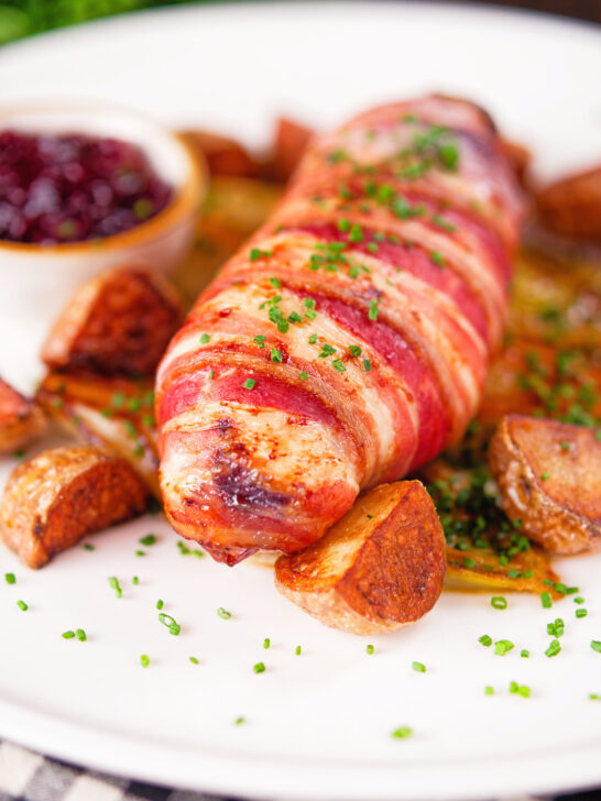 Close-up cranberry and brie stuffed chicken wrapped in bacon with braised chicory and fried potatoes