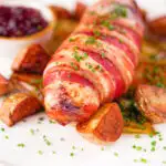 Close-up cranberry and brie stuffed chicken wrapped in bacon with braised chicory and fried potatoes