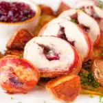Carved cranberry and brie stuffed chicken wrapped in bacon with braised chicory and fried potatoes.