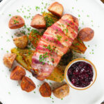 Overhead cranberry and brie stuffed chicken wrapped in bacon with braised chicory and fried potatoes