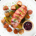 Overhead cranberry and brie stuffed chicken wrapped in bacon with braised chicory and fried potatoes