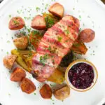 Overhead cranberry and brie stuffed chicken wrapped in bacon with braised chicory and fried potatoes