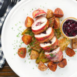 Overhead carved cranberry and brie stuffed chicken wrapped in bacon with braised chicory and fried potatoes.