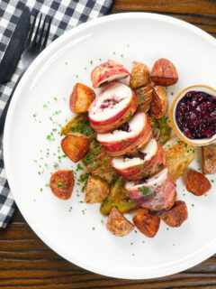 Overhead carved cranberry and brie stuffed chicken wrapped in bacon with braised chicory and fried potatoes.