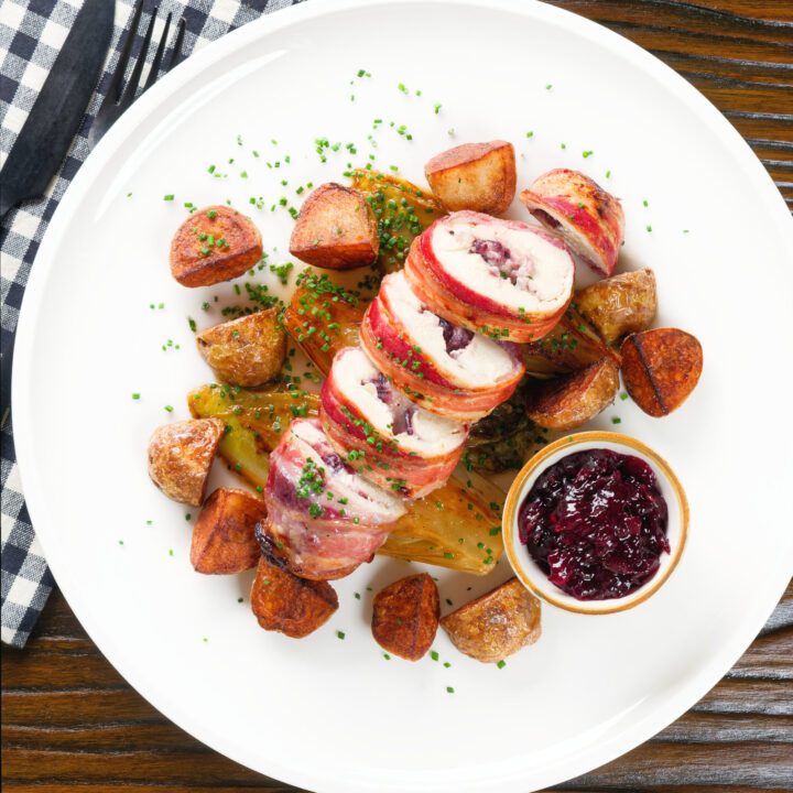 Carved cranberry and brie stuffed chicken breast wrapped in bacon with fried potatoes and white chicory.