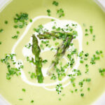 Close-up overhead cream of asparagus soup served with snipped chives and a swirl of cream.