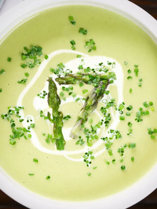 Close-up overhead cream of asparagus soup served with snipped chives and a swirl of cream.