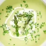 Close-up overhead cream of asparagus soup served with snipped chives and a swirl of cream.