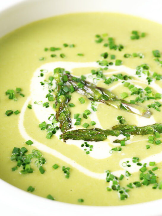 Close-up cream of asparagus soup served with snipped chives and a swirl of cream.