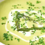 Close-up cream of asparagus soup served with snipped chives and a swirl of cream.