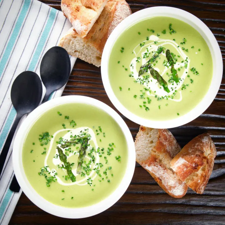 Cream of asparagus soup garnished with asparagus tips, chives and cream served with bread.