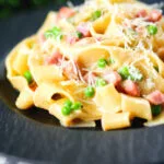 Creamy gammon steak pasta with peas in a carbonara sauce garnished with cheese.