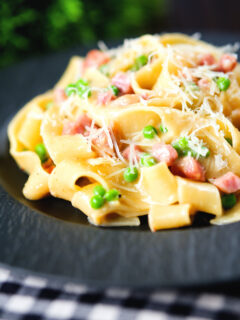 Creamy gammon steak pasta with peas in a carbonara sauce garnished with cheese.