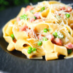 Creamy gammon steak pasta with peas in a carbonara sauce garnished with cheese.