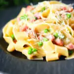 Creamy gammon steak pasta with peas in a carbonara sauce garnished with cheese.