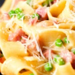 Close-up creamy gammon steak pasta with peas in a carbonara sauce garnished with cheese.