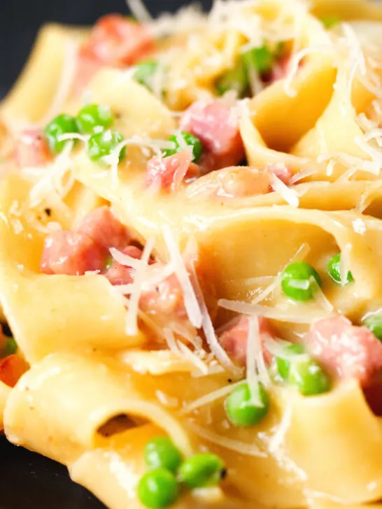 Close-up creamy gammon steak pasta with peas in a carbonara sauce garnished with cheese.