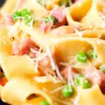 Close-up creamy gammon steak pasta with peas in a carbonara sauce garnished with cheese.