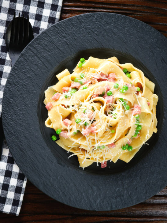 Overhead creamy gammon steak pasta with peas in a carbonara sauce garnished with cheese.