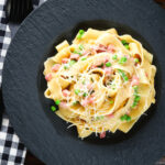 Overhead creamy gammon steak pasta with peas in a carbonara sauce garnished with cheese.