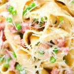 Close-up overhead creamy gammon steak pasta with peas in a carbonara sauce garnished with cheese.