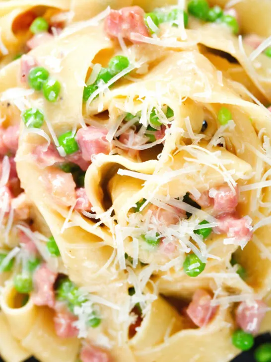 Close-up overhead creamy gammon steak pasta with peas in a carbonara sauce garnished with cheese.