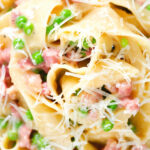 Close-up overhead creamy gammon steak pasta with peas in a carbonara sauce garnished with cheese.