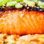 Close-up honey and miso glazed salmon garnished with sesame seeds and spring onions.