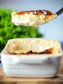 Oven baked British rice pudding being served from its baking dish.