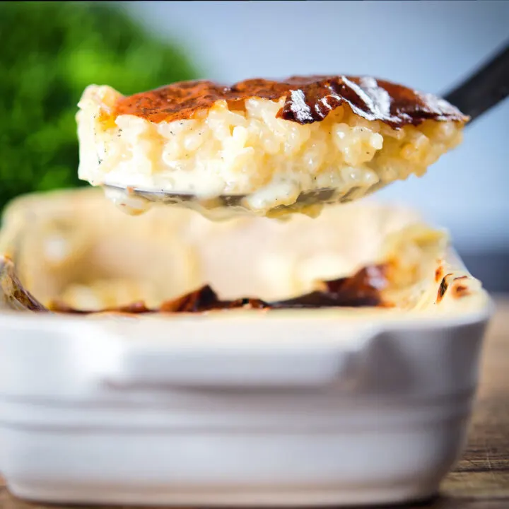 Oven baked creamy rice pudding being served from a baking dish with a spoon.