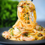 Close-up garlic chilli prawn (shrimp) linguine being picked up with a fork.