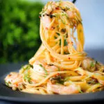 Close-up garlic chilli prawn (shrimp) linguine being picked up with a fork.