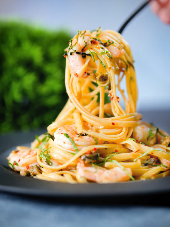 Close-up garlic chilli prawn (shrimp) linguine being picked up with a fork.