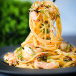Close-up garlic chilli prawn (shrimp) linguine being picked up with a fork.