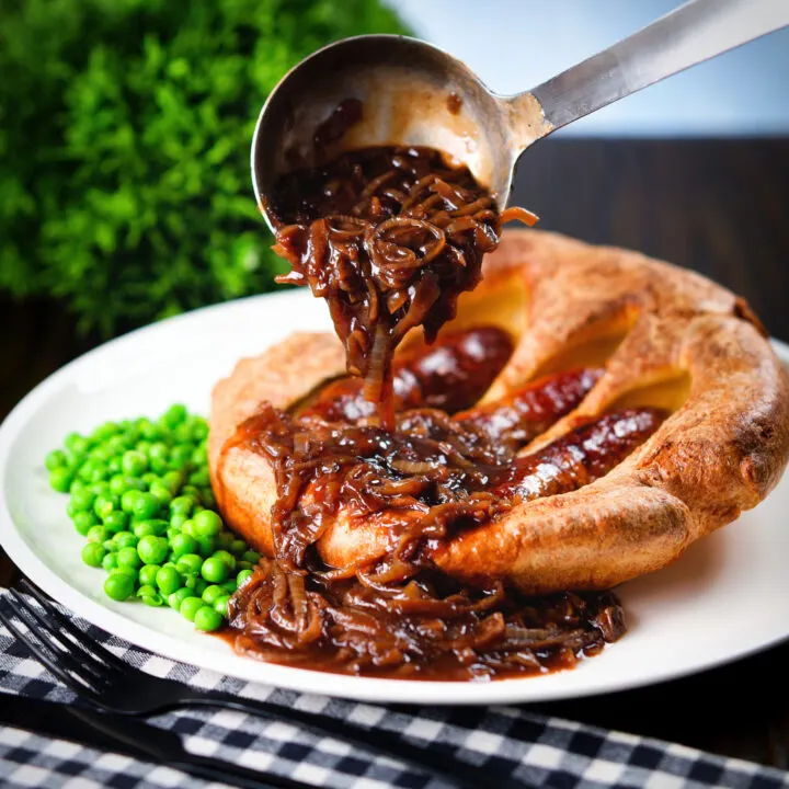 Onion gravy being poured over individual toad in the hole served with peas.