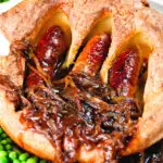 Close-up individual toad in the hole served with peas and a rich onion gravy.