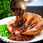 Rich onion gravy being poured over individual toad in the hole served with peas.