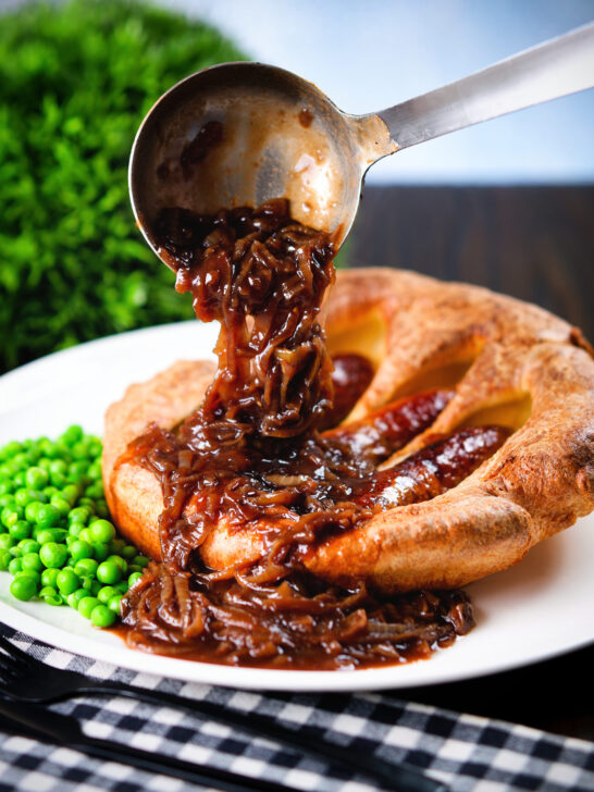 Rich onion gravy being poured over individual toad in the hole served with peas.