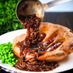 Rich onion gravy being poured over individual toad in the hole served with peas.